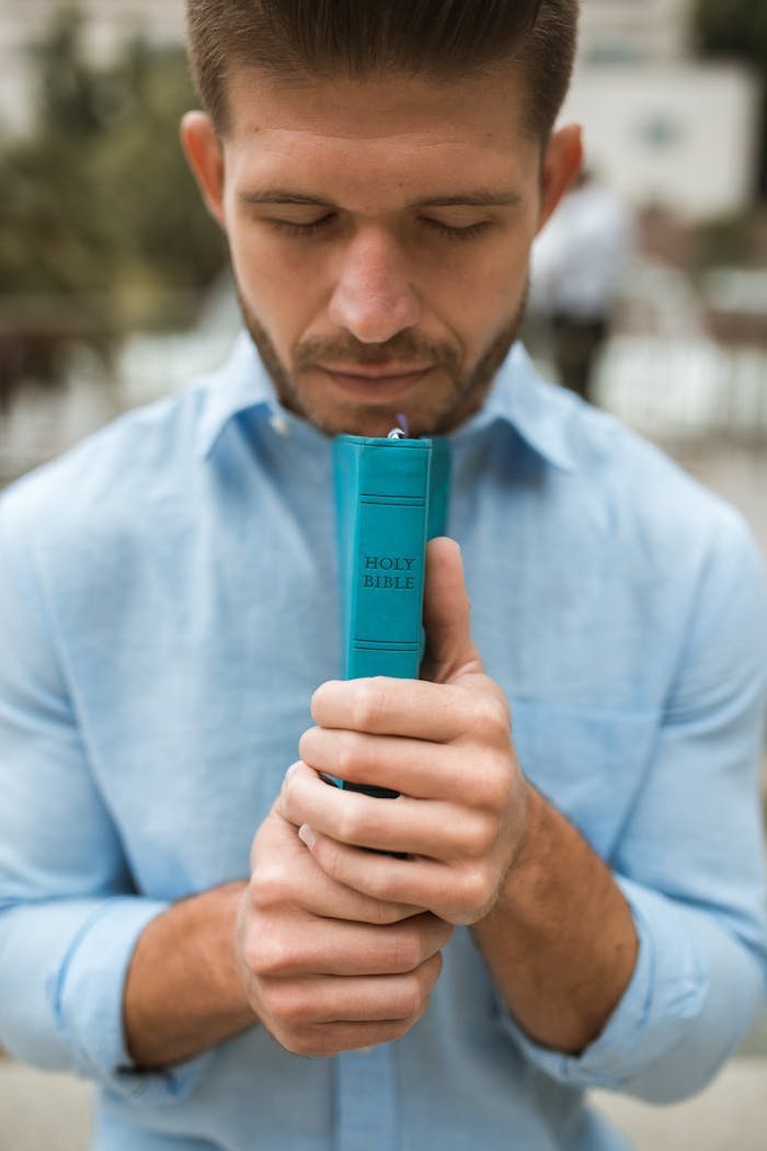 Adult male praying outdoors with Holy Bible, conveying faith and spirituality.